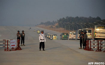 Burmese policemen man a check-point on a road leading to the national parliament as shuttle buses (R) carry Members of Parliament to the newly-completed compound after inspection, in the capital Naypyidaw on January 31, 2010. Burma's new junta-dominated parliament opened on January 31 as lawmakers assembled in secrecy for their first legislative session since the late 1980s following a widely panned election. After a rare election in November, marred by the absence of democracy icon Aung San Suu Kyi and claims of cheating and intimidation, the junta was set to easily dominate Burma's first parliamentary session in two decades. AFP PHOTO