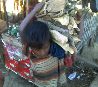 A small boy carries firewood to his hut. He has never attended school.