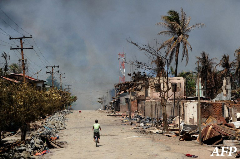 This file picture taken on June 12, 2012, shows a resident riding her bicycle past burned houses amid ongoing violence in Sittwe, the capital of Rakhine State in Burma.