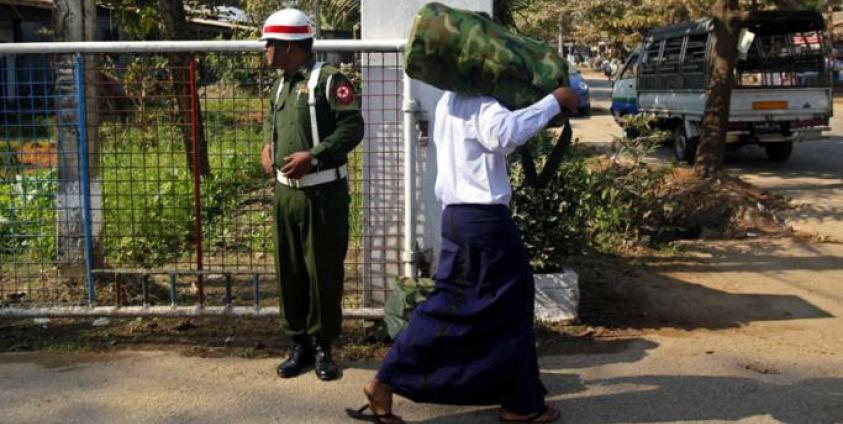 (File) Myanmar boy wearing a white shirt (R), who was discharged from Myanmar army, loads a bag on his shoulder as he walks near a military man at a gate of military compound - 18 January 2014. Photo: Lynn Bo Bo/EPA