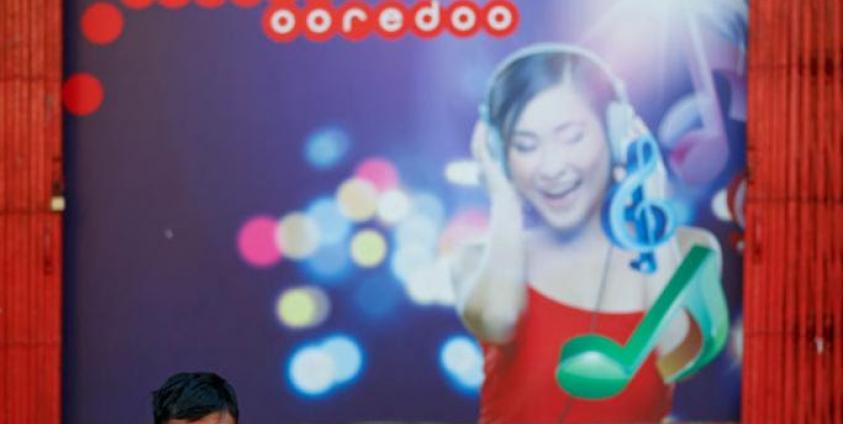 A man speaks on his mobile phone in front of a building with Ooredoo telecom advertising at downtown area in Yangon. Photo: Lynn Bo Bo/EPA