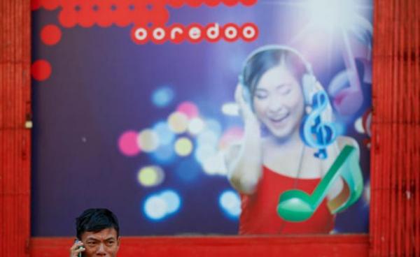 A man speaks on his mobile phone in front of a building with Ooredoo telecom advertising at downtown area in Yangon. Photo: Lynn Bo Bo/EPA